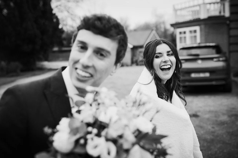 A laughing couple holding flowers outside The Norfolk Mead, photographed in black and white